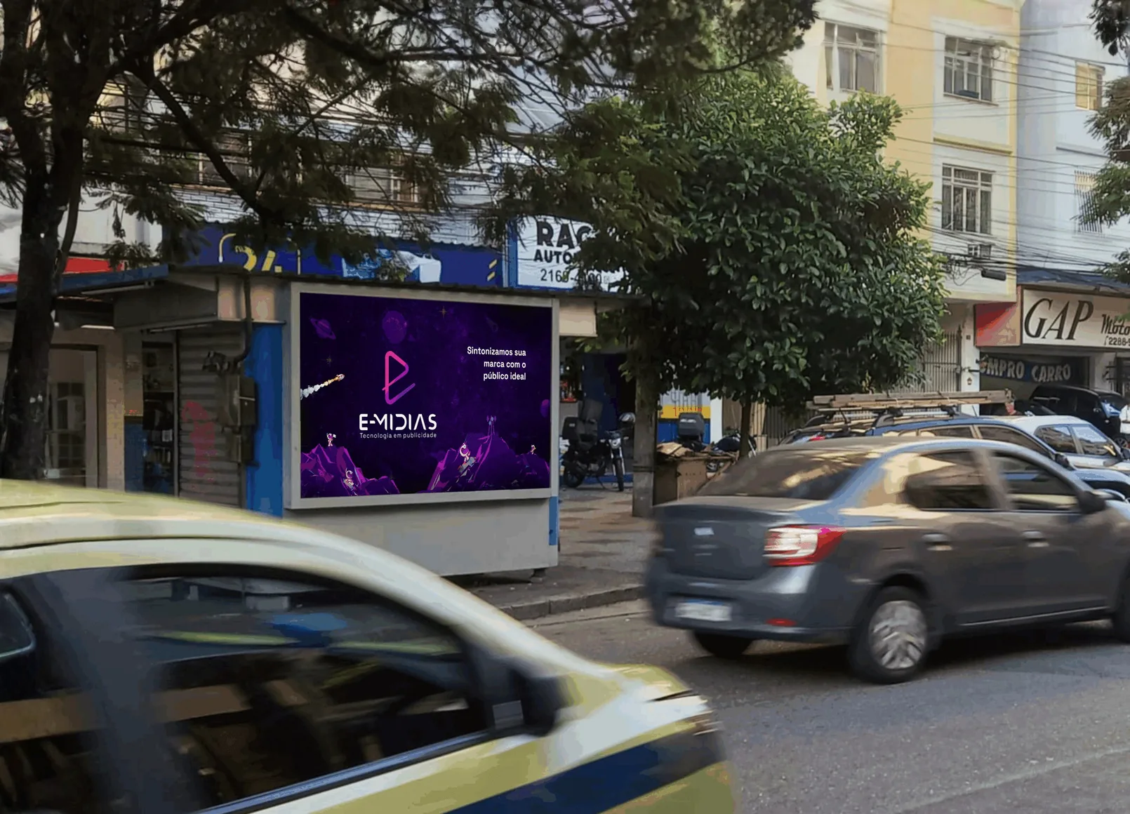 Painel de mídia exterior da E-Mídias numa avenida movimentada, com um carro passando
